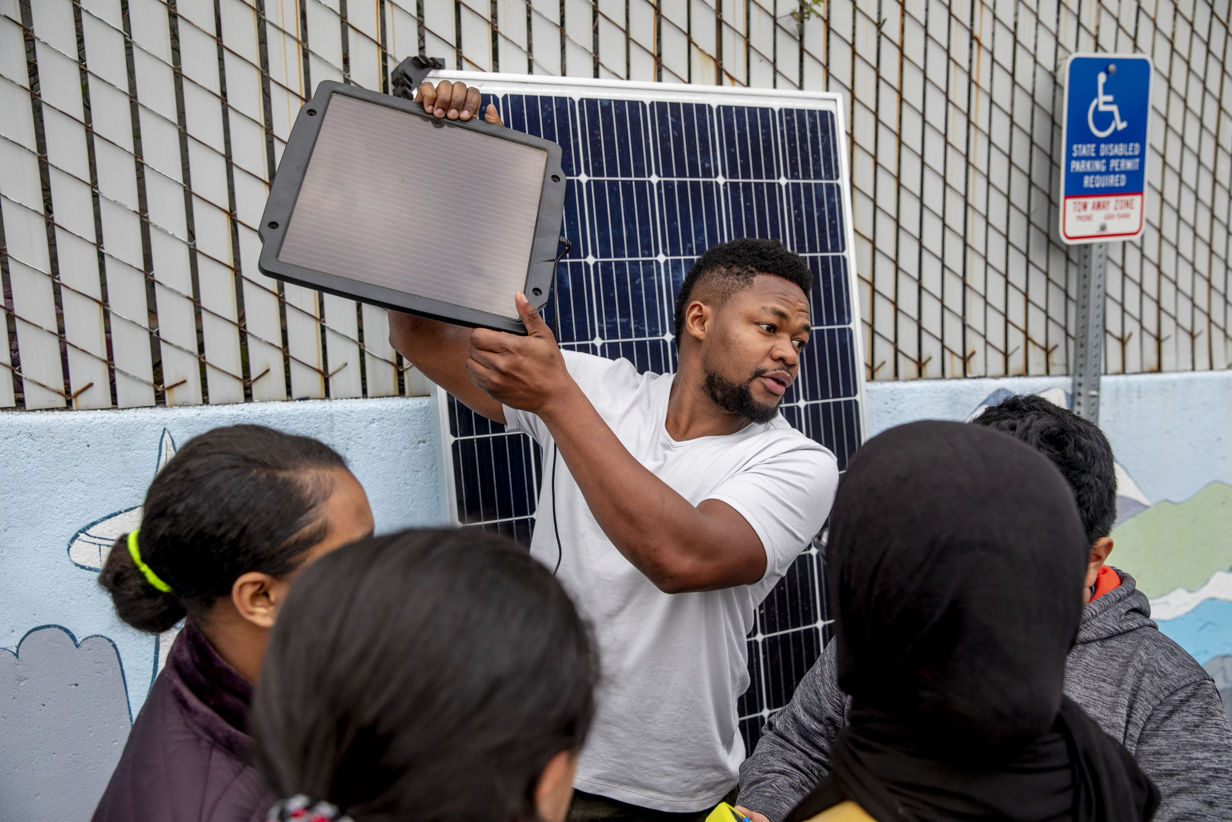  Edwin Wanji, center, teaches a group of kids from the Lake City Young Leaders program about how to work a solar panel at the Lake City Community Center on April 1. Wanji is the owner and founder of Sphere Solar Energy in Seattle and is often invited to talk to students about opportunities in solar. "I'm trying to create excitement around this field. It's renewable energy, it's exciting, there will always be more sunlight tomorrow," he says. "It's encouraging to see the kids' excitement about it." (Photo by Dorothy Edwards/Crosscut)
