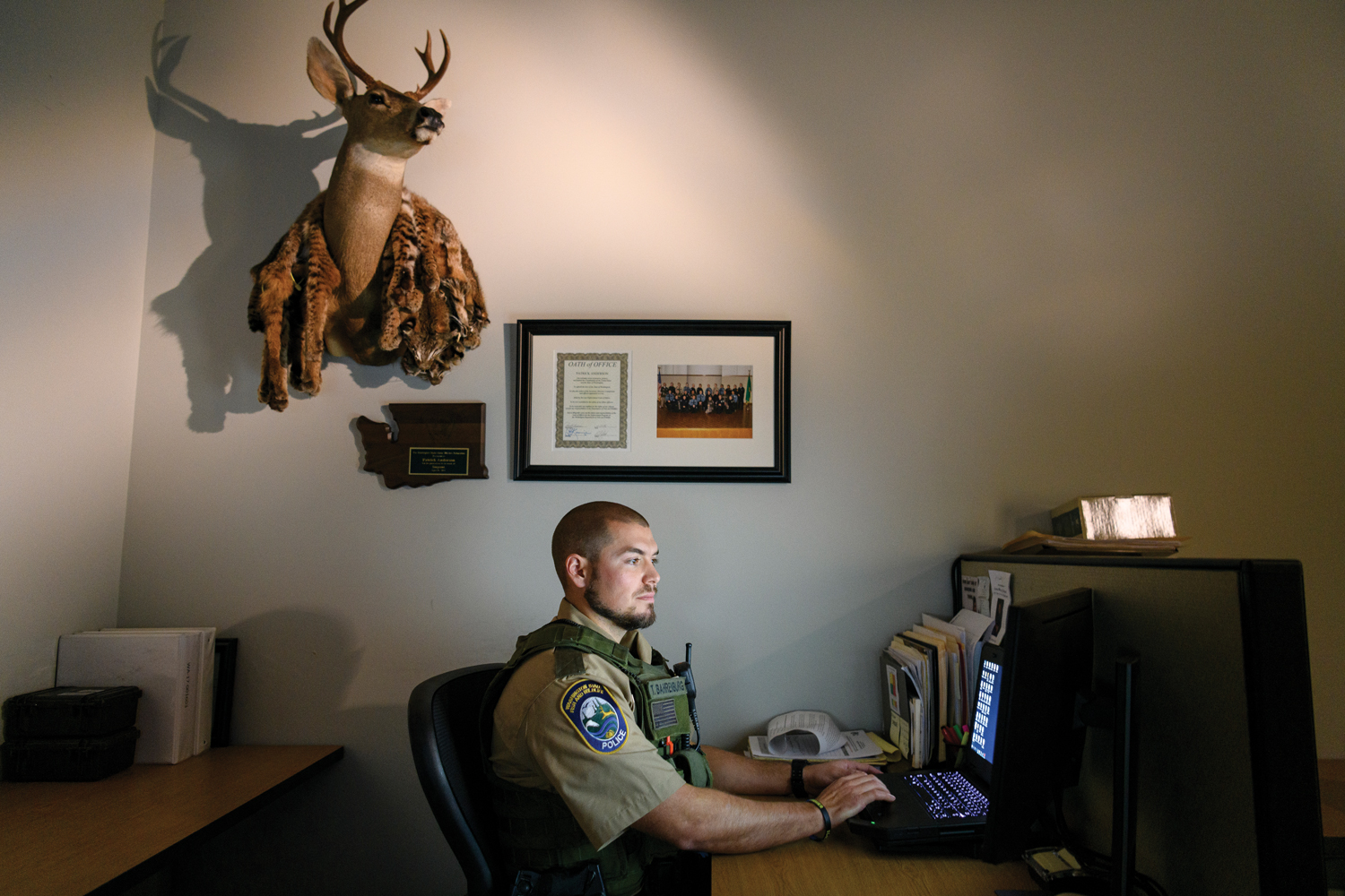 Officer Tyler Bahrenburg sits at his computer. A mounted deer head hangs on his office wall