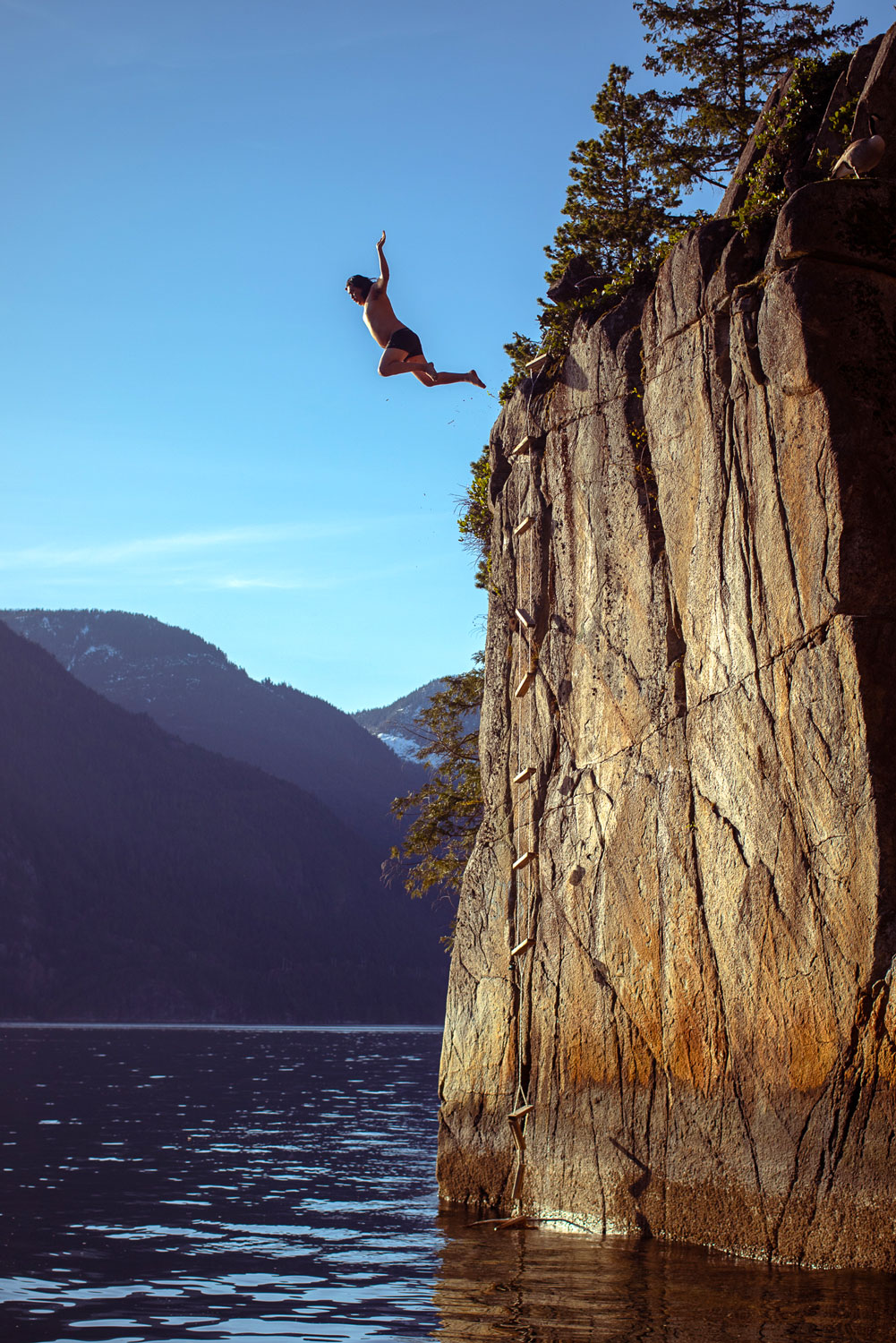 A person in swim trunks jumps from a cliff into the ocean