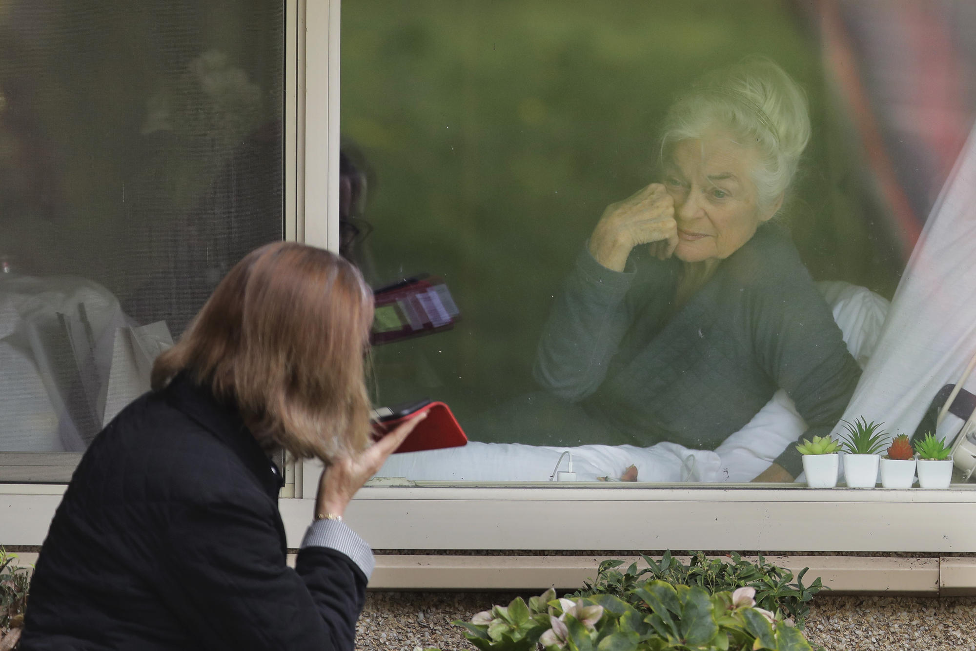 A coronavirus patient visits with her daughter through a window