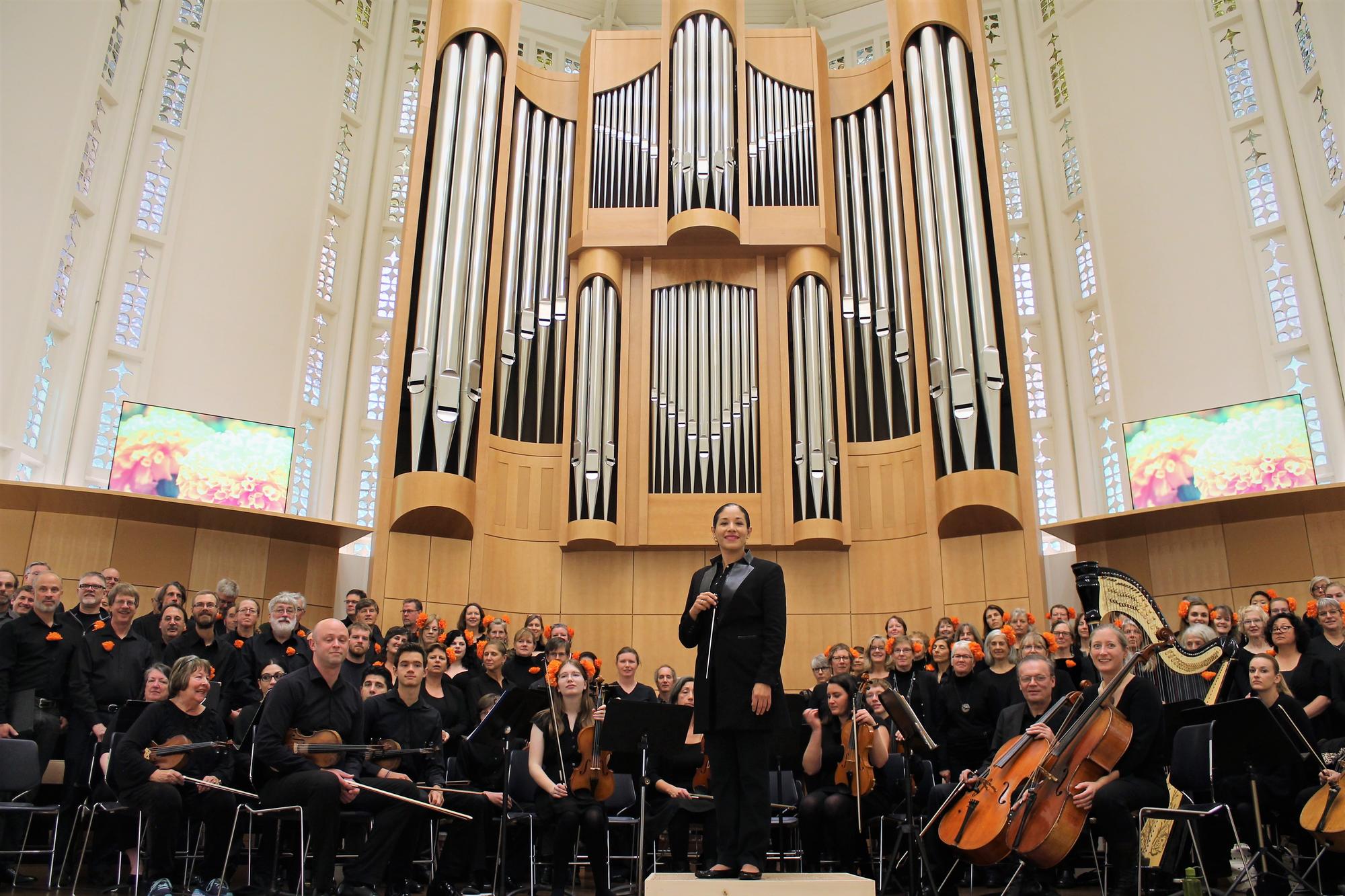 Paula Nava Madrigal stands amid an orchestra in front of a large concert organ