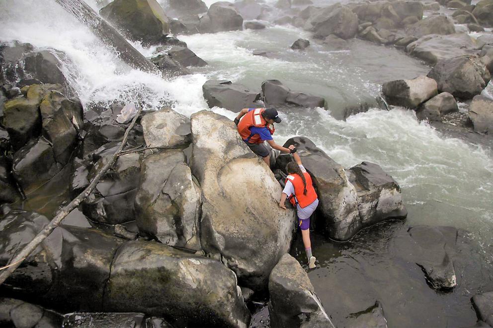 View of two people climbing over boulders in a flowing river