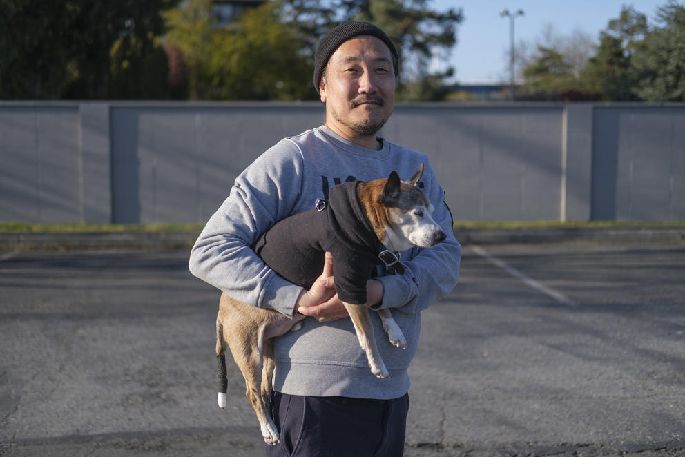 Man with hat holds a dog in empty parking lot