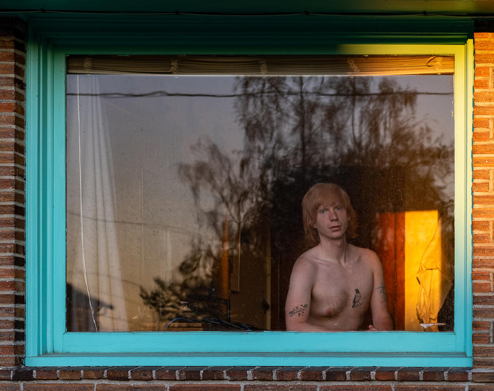 Shirtless person sitting behind a window