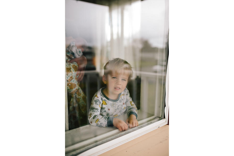 Kid in pajamas looks at camera from behind a window