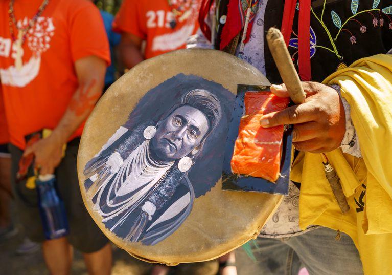 Hands holding a drum with a Native portrait painted on it and a vacuum-packed piece of salmon