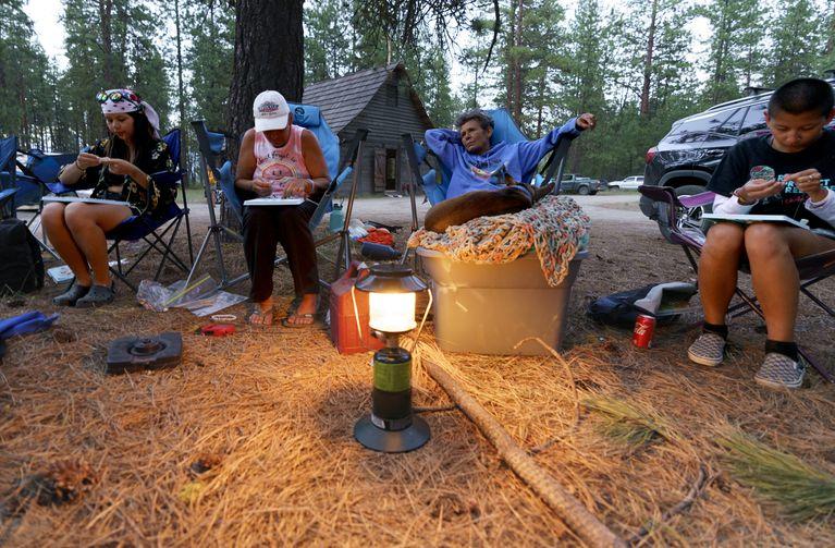 People sit in camp chairs around a lantern