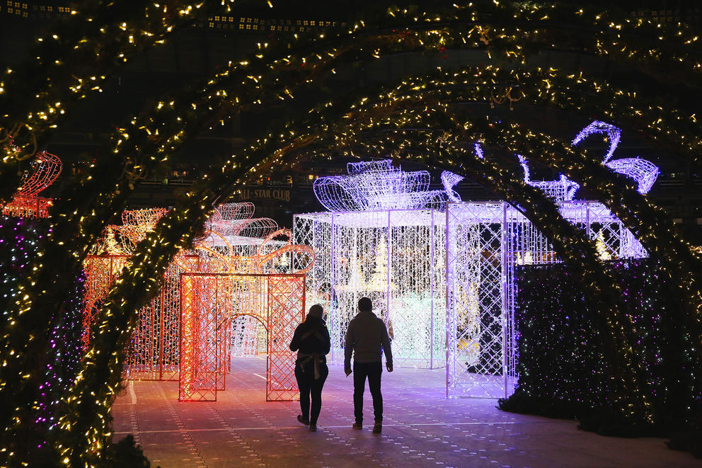 Two silhouetted figures walk through a Christmas light maze
