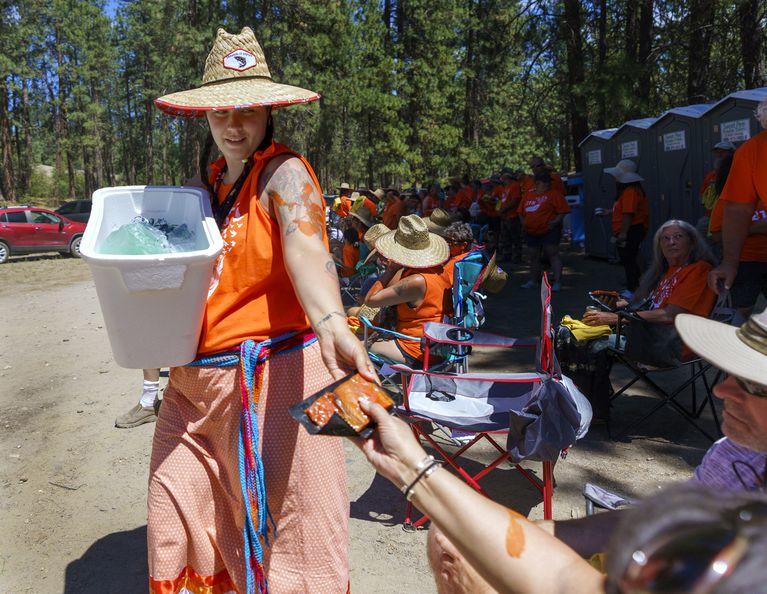 A woman holding a bucket hands out vacuum-packed salmon to people sitting in camp chairs