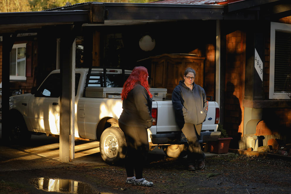 Destiny Armstrong and her daughter Katelin Rayment stand in the driveway of their home against a white pickup truck in a carport