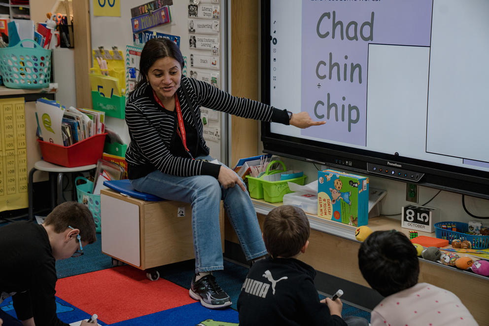 A teaching professional points to words that start with the letters "ch" while three students watch.
