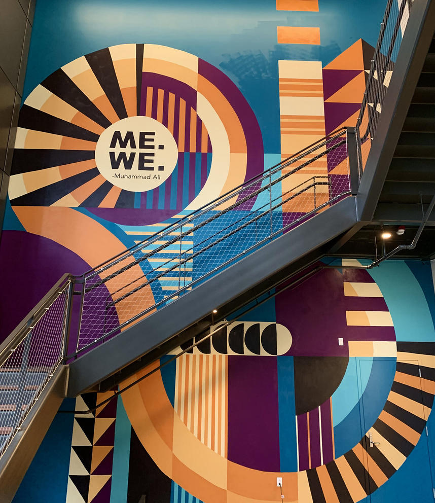 a two-story mural featuring turquoise and orange swirling stripes that reads Me, We