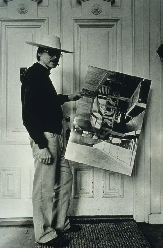 a black and white photograph of a man in a hat holding up a large image of an artwork