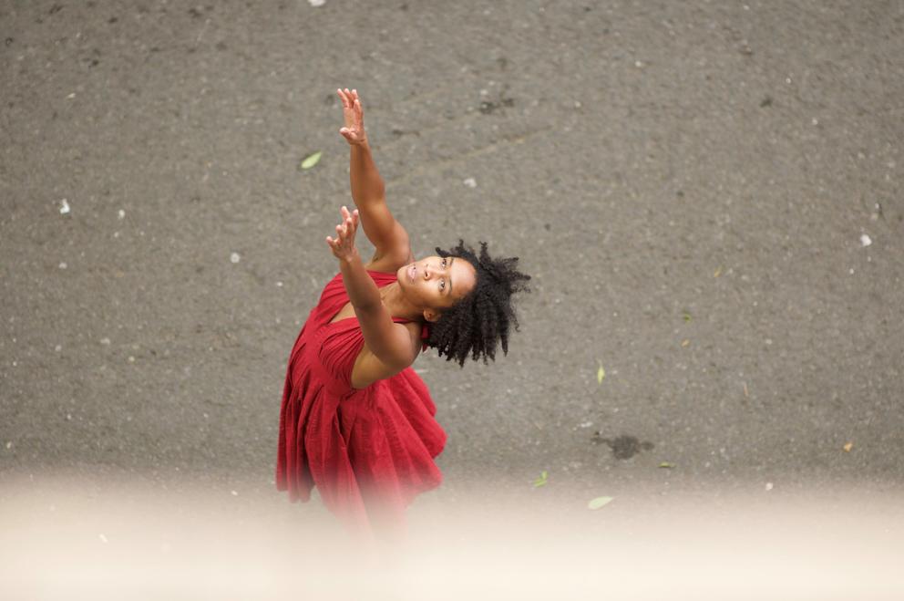 a dancer in a red dress reaches her arms and face to the sky
