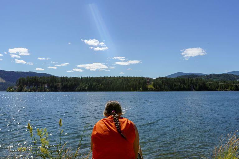 A person with their back turned toward the camera looking out at a lake