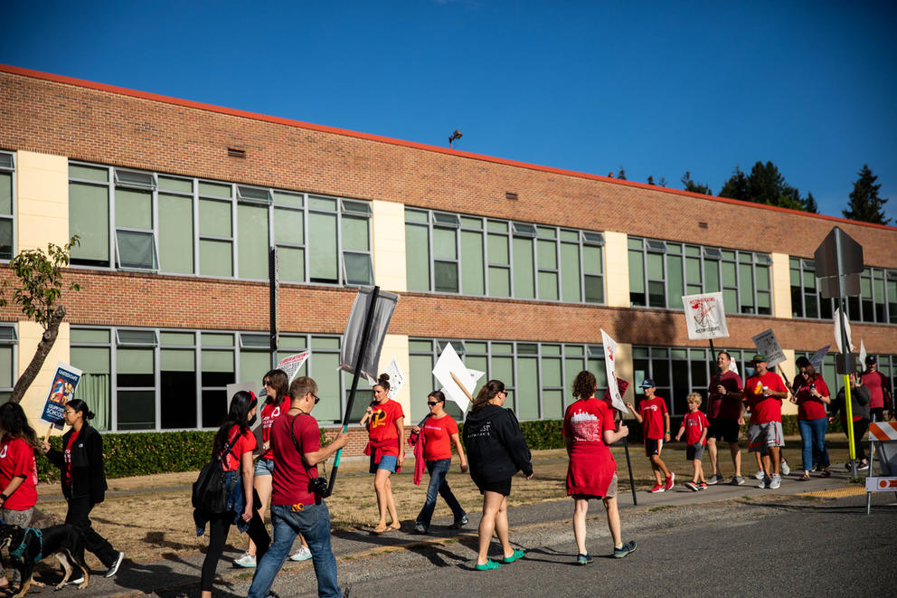 Marchers wearing red carry signs in front of a school.