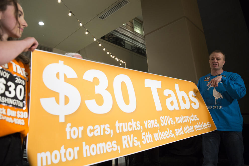 Tim Eyman holds a $30 car tab sign