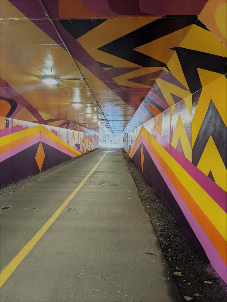 photo of a long bike tunnel painted in geometric patterns in yellow, purple and pink