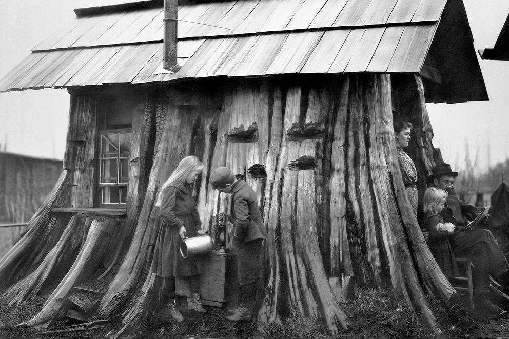A family outside a house built from a tree stump.