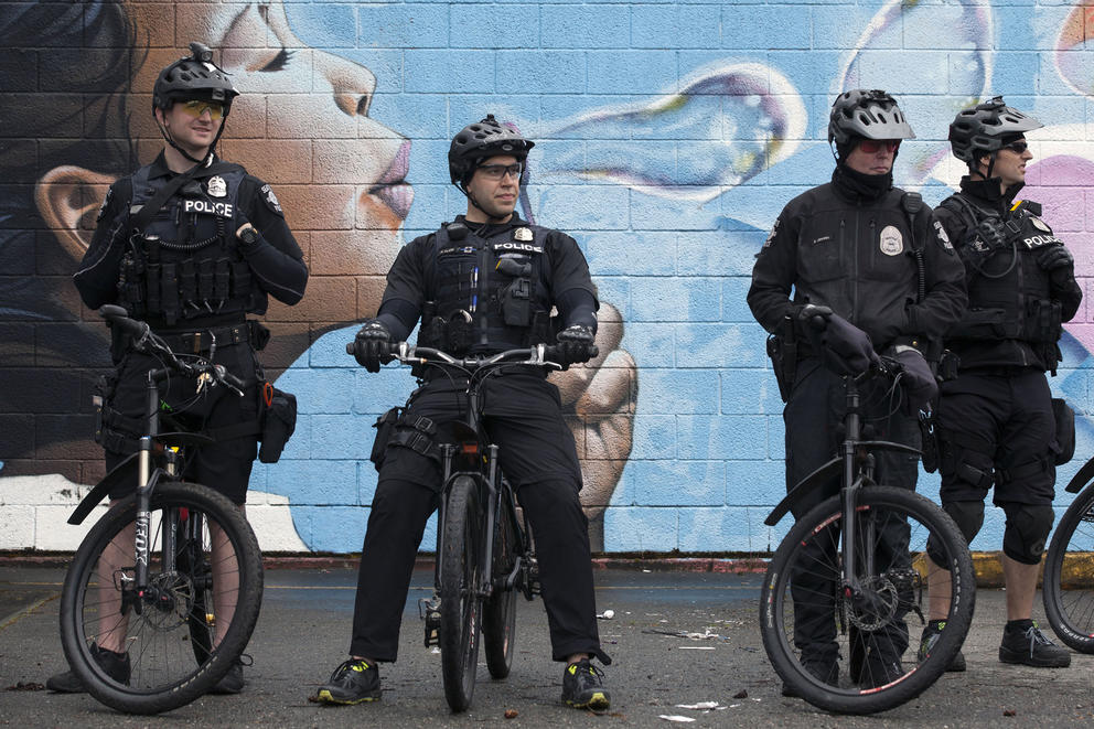 Four officers on bikes stand at rest in front of a blue mural