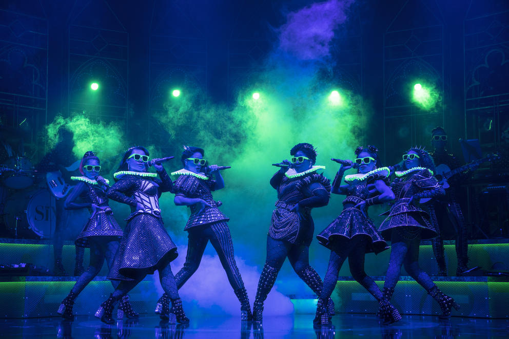 a theatrical stage moment with six women doing a dance move under dramatic lights