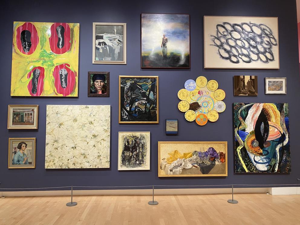 a gallery wall with colorful paintings in all sizes hung closely together
