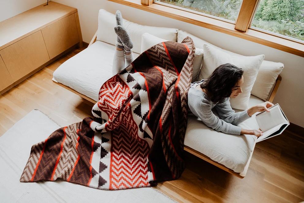 press photo of a woman on a couch draped in a native-made blanket