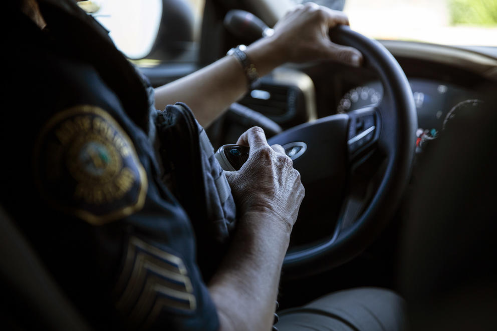 Portland, Oregon police officer has one hand on a steering wheel and the other on a communication device as she drives.