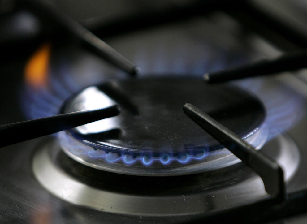 A close up image of a gas stove burner emitting blue flames 