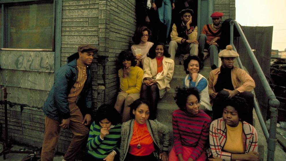 a movie still with Black 1960s teenagers sitting on a stoop