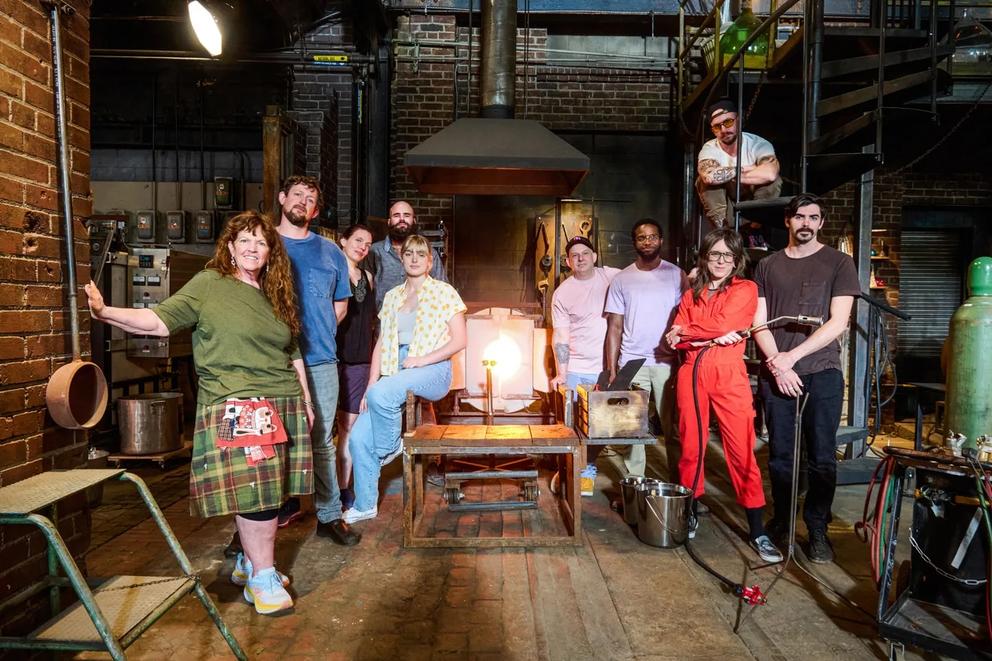 a group photo of several people in a glassblowing studio standing around a flame