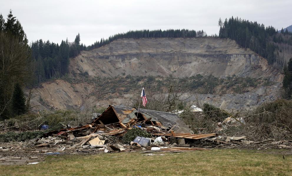 A flag is seen in the ruins of a home seen in front of a barren hillside.