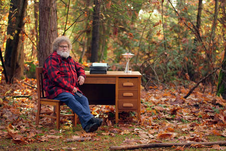 Knute Berger sits at a desk in the woods among fallen leaves