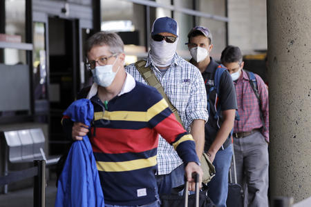 Travelers wear protective masks as they wait for a shuttle after arriving at Seattle-Tacoma International Airport