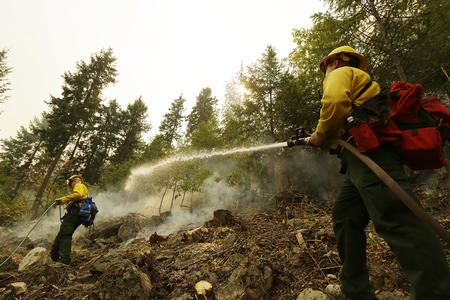 Colby Lyon, of the Central Region Strike Force Team II, sprays a hillside with water as part of the response to a fire near Chelan, Wash. on Aug. 18, 2015.