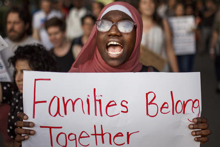 woman in hijab holds sign that reads "families belong together"