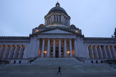The Washington State Legislative Building and its dome are silhouetted as the light dims and a jogger passes by the building's stone steps