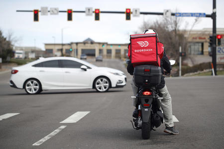a door dash delivery person sits on a scooter at a red light