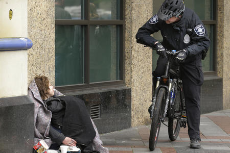 Seattle police officer on a bike speaks to women sitting on the sidewalk