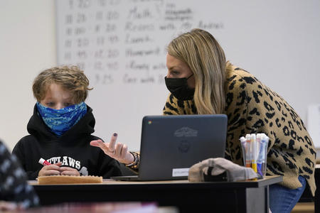 A teacher and student sit together wearing face masks