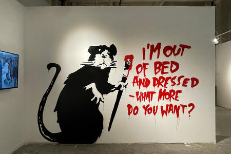 white wall featuring a large rat with a brush in its hands, with text saying: "I'm out of bed and dressed, what more do you want?"