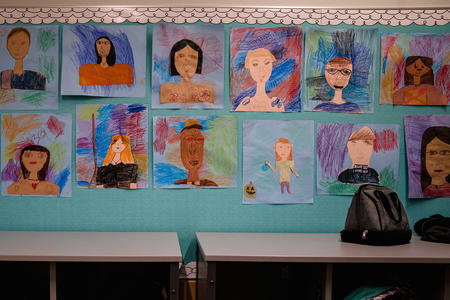 Paintings of different faces adorn a wall at a school.