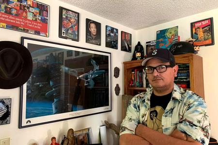 Jeffrey Veregge crosses his arms in front of wall of framed geeky artifacts