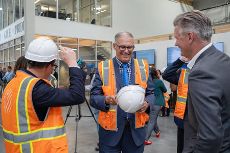 Gov. Jay Inslee wears a safety vest and holds a hard hat before a tour of the Katerra mass timber factory.