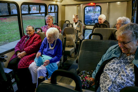 Seven older women enjoy a laugh while riding in a transit van