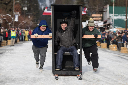An outhouse sitter pumps his fist in the air while approaching the finish line, flanked by pushers during the Outhouse Races in Conconully, Wash. on Saturday, Jan. 19, 2019. 