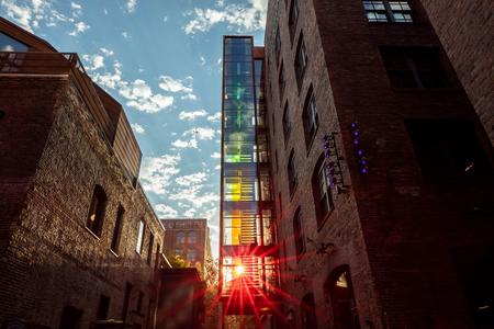 two brick buildings with a stairwell lit in rainbow colors in between