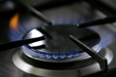 A close up image of a gas stove burner emitting blue flames 