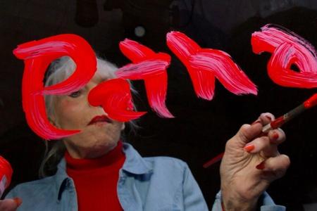 photo of a white haired woman painting the name PATHA in pink on glass