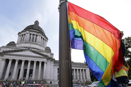 A state worker unfurls a rainbow flag in front of the Washington state Capitol 